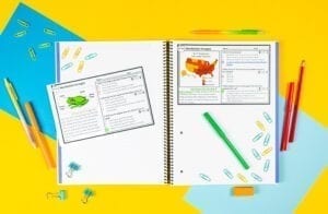 Notebook showing two exit ticket passages. One has an image of a frog and then other a map of the united states. The text is illegible because it is small. There are pencils and pens laying around the passages which are set atop an open notebook along with paper clips.