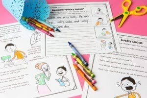 Printed pages containing stories with illustrations colored with crayons that are laying across pages with a pink background under the pages