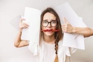 Teacher holding lots of paper and a pen in her mouth looking anxious about closing testing gaps before standardized testing