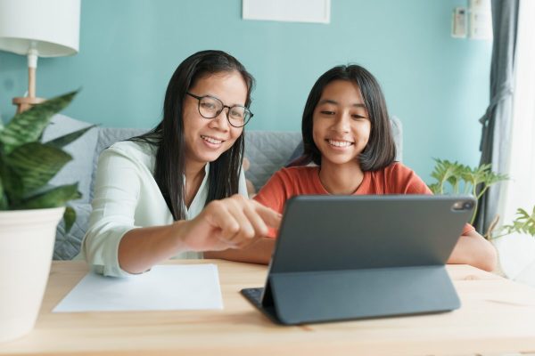 Asian family with a daughter do homework by using tablet with mother help. Happy smile Asia kid while sitting in the living room at home morning. Concept of online learning at home